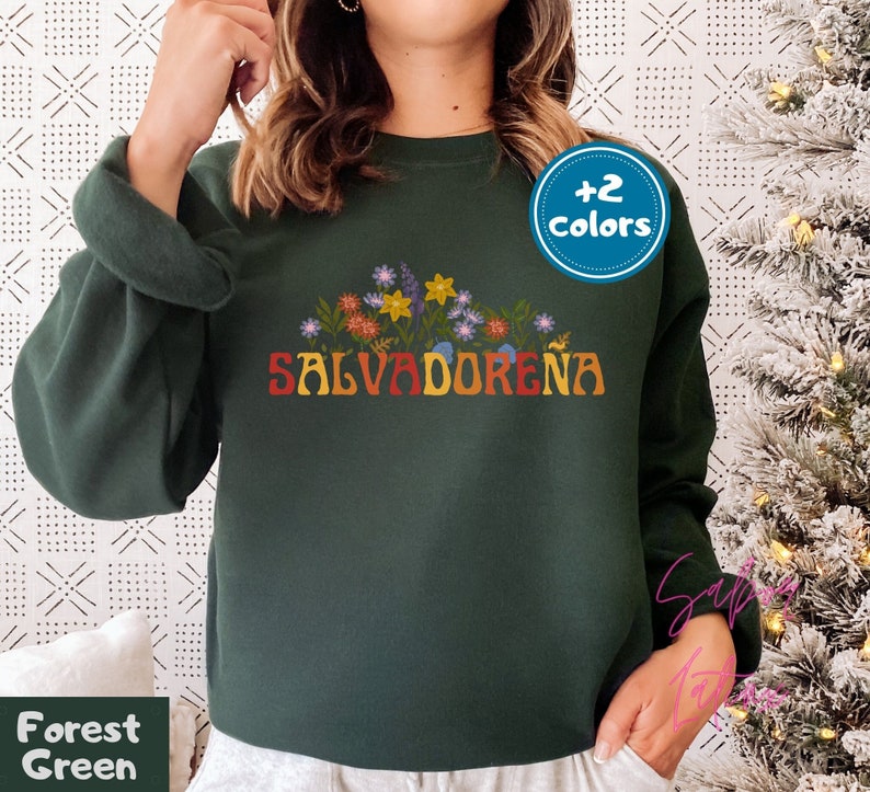 May include: A forest green sweatshirt with the word "SALVADORENA" in rainbow letters and a floral design above the text. The sweatshirt is available in two colors.