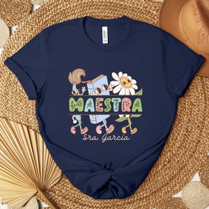 Peut inclure: Un t-shirt bleu marine avec un graphique repr&eacute;sentant un livre, des fleurs et le mot "MAESTRA" avec le texte "Sra. Garcia" en dessous.