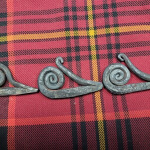 May include: Three metal fire starters shaped like snails, with a spiral design. The fire starters are on a red and black plaid fabric.