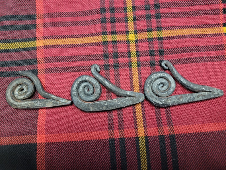 May include: Three metal fire starters shaped like snails, with a spiral design. The fire starters are on a red and black plaid fabric.