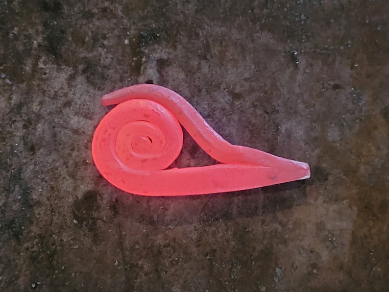 May include: A red-hot metal spiral, forged in a blacksmith's fire, is shaped into a unique design. The metal glows with a bright orange hue, highlighting the intricate details of the spiral.