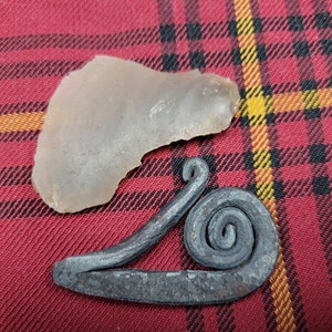 May include: A gray flint stone and a metal fire starter with a spiral design on a red and black plaid fabric background.
