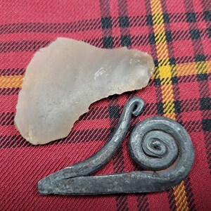 May include: A gray stone and a metal snail-shaped fire starter on a red and black plaid fabric.