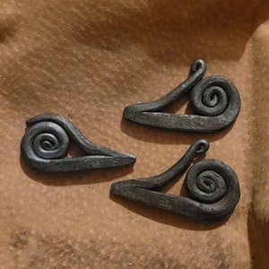 May include: Three black metal snail sculptures on a brown paper background. Each snail has a curled shell and a long, thin body.