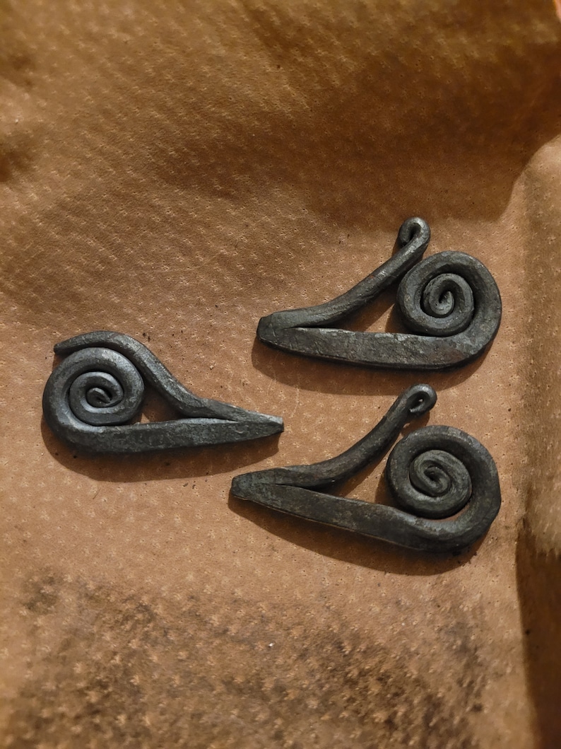 May include: Three black metal snail sculptures on a brown paper background. Each snail has a curled shell and a long, thin body.