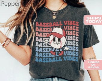Op de afbeelding: Een donkergrijs T-shirt met een vintage-stijl baseball-afbeelding en de tekst "BASEBALL VIBES" die herhaald wordt in een regenboogkleurenschema.