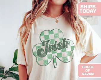 May include: A white t-shirt with a green shamrock design. The shamrock is checkered with green and white squares. The word "Irish" is written in a green retro font inside the shamrock. The shirt has a distressed look.