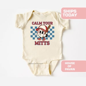 May include: A cream-colored baby onesie with short sleeves features a cartoon baseball with a red cap and a bat. The baseball has a face and is wearing red shoes. The text "Calm Your Mitts" is printed on the onesie.