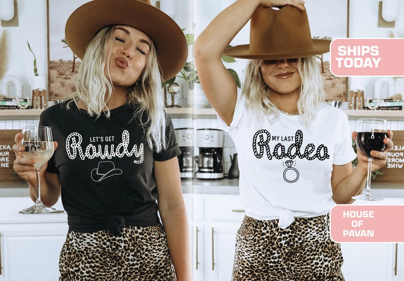 May include: Two women wearing black and white t-shirts with a western theme. The black shirt says "Let's Get Rowdy" with a rope design and a cowboy hat. The white shirt says "My Last Rodeo" with a rope design and a diamond ring. Both women are wearing brown cowboy hats and leopard print skirts.