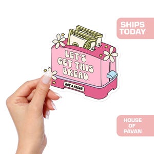 May include: Pink toaster with the text "Let's Get This Bread" and the words "Hot & Fresh" printed on the front.  The toaster has money inside and flowers on top.