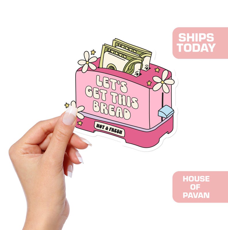Puede incluir: Tostadora rosa con el texto "Let's Get This Bread" y las palabras "Hot & Fresh" impresas en la parte delantera. La tostadora tiene dinero dentro y flores en la parte superior.