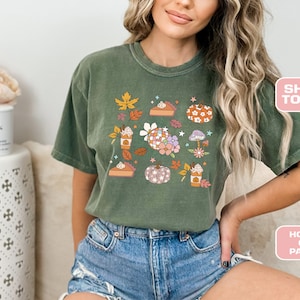 May include: A green t-shirt with a fall-themed design featuring pumpkins, pie, coffee cups, and leaves. The design is in a retro style with a patchwork pumpkin and a coffee cup with whipped cream.
