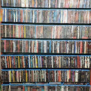 May include: A large collection of Blu-ray discs, arranged on shelves. The spines display a variety of colours and titles, suggesting a diverse selection of films and TV shows. The cases have a blue border.