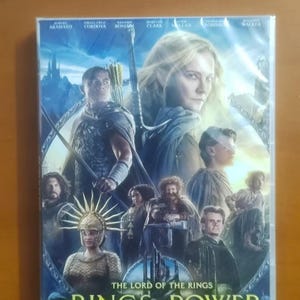 K&ouml;nnte beinhalten: DVD-H&uuml;lle f&uuml;r "Der Herr der Ringe: Die Ringe der Macht - Staffel 1". Das Cover zeigt Charaktere vor einer Fantasy-Landschaft. Der Titel ist in einer stilisierten Schriftart dargestellt.