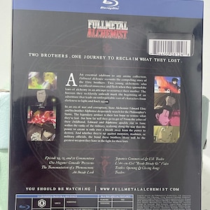 K&ouml;nnte beinhalten: Fullmetal Alchemist Blu-ray Box-Set mit einem dunkelblauen Hintergrund und einem silbernen und schwarzen Bild von zwei Br&uuml;dern. Das Box-Set enth&auml;lt sechs Blu-ray-Discs und hat eine Laufzeit von 1275 Minuten. Die R&uuml;ckseite der Box enth&auml;lt eine Beschreibung der Anime-Serie und eine Liste der Sonderfunktionen.