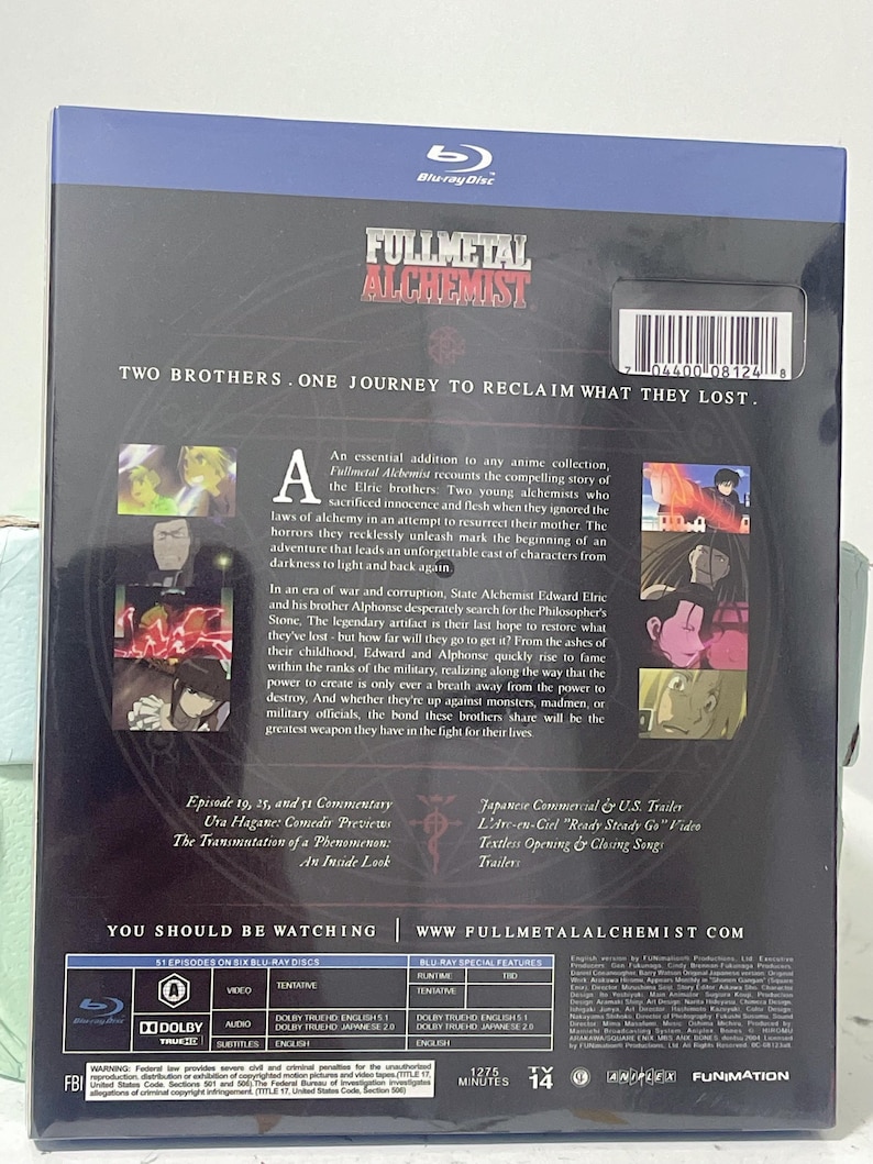 K&ouml;nnte beinhalten: Fullmetal Alchemist Blu-ray Box-Set mit einem dunkelblauen Hintergrund und einem silbernen und schwarzen Bild von zwei Br&uuml;dern. Das Box-Set enth&auml;lt sechs Blu-ray-Discs und hat eine Laufzeit von 1275 Minuten. Die R&uuml;ckseite der Box enth&auml;lt eine Beschreibung der Anime-Serie und eine Liste der Sonderfunktionen.
