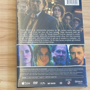 May include: DVD case for the television series "Slough House" featuring a cast photo. The back of the case includes a plot summary and details about the episodes, audio, and subtitles. The case is sealed in plastic.