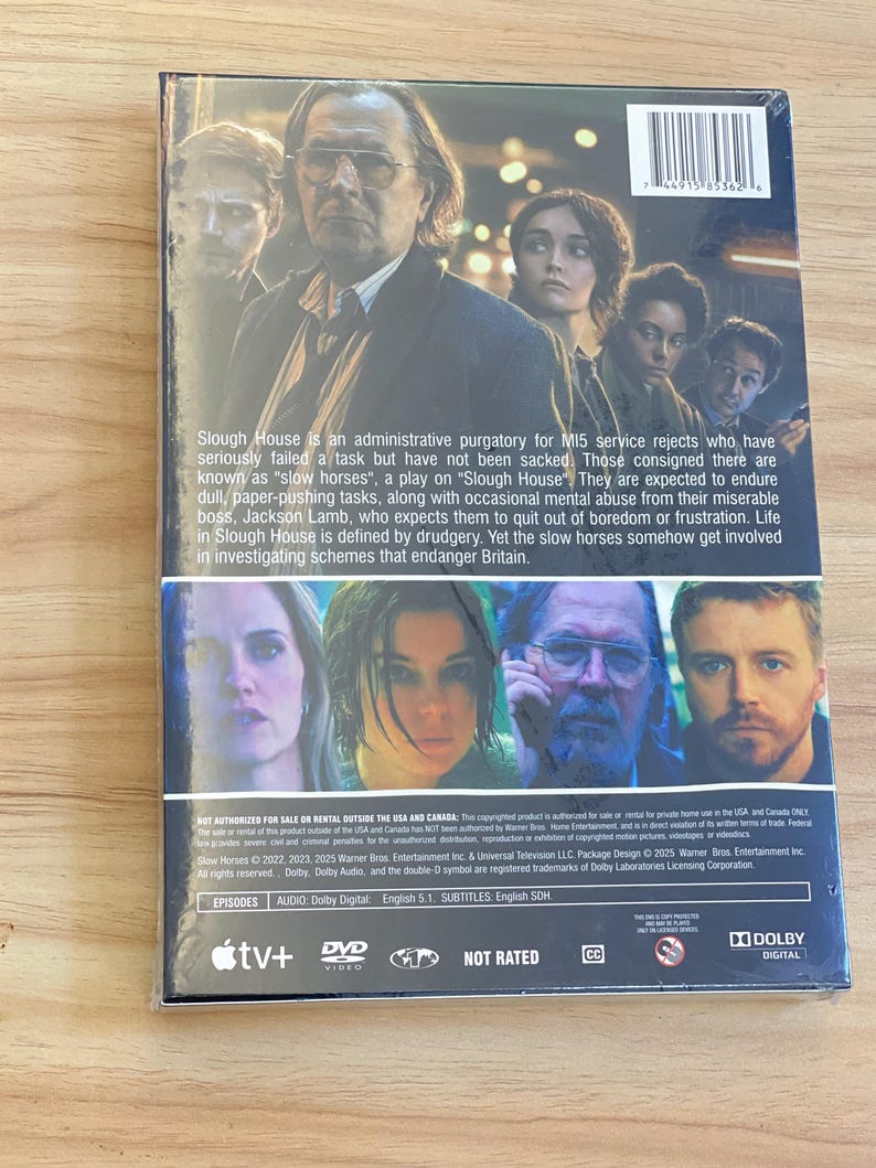 May include: DVD case for the television series "Slough House" featuring a cast photo. The back of the case includes a plot summary and details about the episodes, audio, and subtitles. The case is sealed in plastic.