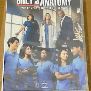 Peut inclure: Boîtier DVD de Grey's Anatomy : La Dix-neuvième Saison Complète. La couverture présente un groupe d'acteurs en tenues médicales et professionnelles. Le titre de l'émission est affiché en grandes lettres en haut.