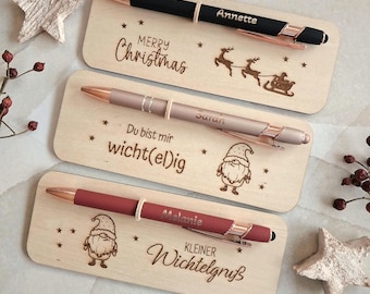 May include: Three pens with rose gold accents, each resting on a rectangular wooden plaque. The top pen is black with the name Annette, the middle is light brown with the name Sarah, and the bottom is dark red with the name Melanie.