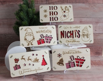May include: A collection of wooden Christmas signs with laser-cut designs and text. The signs feature festive images like a snowman, Santa, gifts, and the words "HO HO HO" and "Merry Christmas".