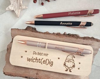 May include: Three ballpoint pens with rose gold accents and personalized names, including Melanie, Annette, and Sarah. One pen rests on a rectangular wooden plaque engraved with the German text "Du bist mir wicht(el)ig" and a gnome illustration.