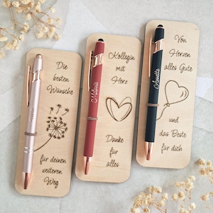 Op de afbeelding: Drie rechthoekige houten bladwijzers, elk met een pen. De eerste heeft een roségouden pen en paardenbloemafbeelding met Duitse tekst. De tweede heeft een matte rode pen, hartafbeelding en Duitse tekst. De derde heeft een zwarte pen, ballonafbeelding en Duitse tekst.