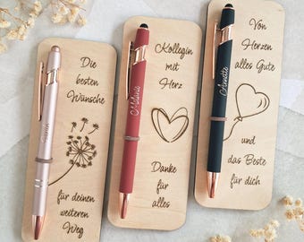 Könnte beinhalten: Drei rechteckige Lesezeichen aus hellem Holz, jedes mit einem Stift in einer kleinen Schlaufe. Das erste hat einen roségoldenen Stift und eine Pusteblume. Das zweite einen roten Stift und ein Herz. Das dritte einen schwarzen Stift und einen Ballon.