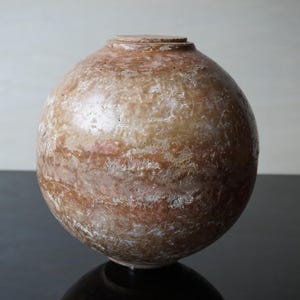 Op de afbeelding: Een bolvormige, getextureerde vaas met lichtbruine en roodbruine tinten. De vaas heeft een kleine, platte bovenkant en een afgeronde body. Het oppervlak heeft een verweerde uitstraling, met variaties in kleur en textuur.