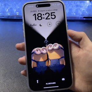Könnte beinhalten: Ein Smartphone mit einem schwarzen Bildschirm, auf dem eine Digitaluhr 18:25 anzeigt, der Text "have a nice day" und zwei gelbe Minions-Figuren, die eine Taschenlampe halten. Das Telefon hat eine weiße Hülle.