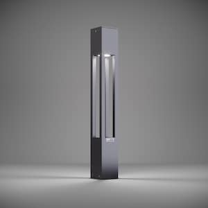 May include: A modern, black outdoor light fixture with a rectangular shape and a clear glass panel. The light is on and illuminating the surrounding area.