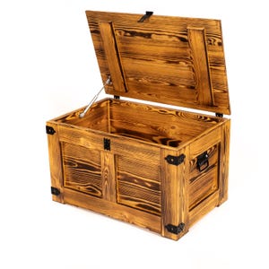 Può includere: Uno scrigno in legno con un coperchio incernierato e dettagli in metallo. Lo scrigno è realizzato in legno riciclato e ha un aspetto rustico e vissuto.