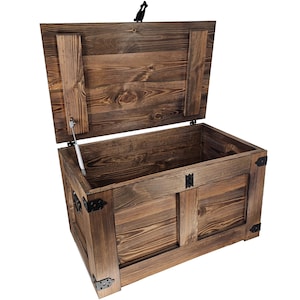 Op de afbeelding: Een houten opbergkist met een scharnierend deksel en metalen accenten. De kist is gemaakt van donkerbruin hout en heeft een rustieke uitstraling.