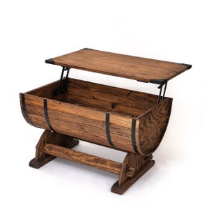 May include: A brown wooden coffee table constructed from a barrel shape with a lift-top mechanism. The table features dark metal bands around the curved body, a rectangular wooden top, and a sturdy base with two side supports for stability.
