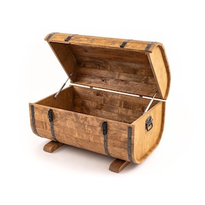 Op de afbeelding: Een houten kist met een scharnierend deksel, open om de binnenkant te onthullen. De kist is tonvormig met metalen banden en hardware. Hij staat op twee houten steunen. Het hout heeft een warme, natuurlijke afwerking.