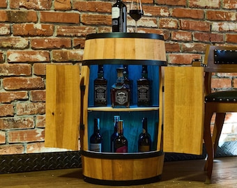 May include: A wooden barrel-shaped bar cabinet with two doors. The cabinet has a glass shelf with four bottles of spirits and a second shelf with four bottles of wine. The cabinet is lit with blue LED lights.