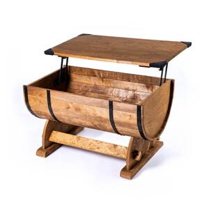 Peut inclure: Une table basse en bois en forme de tonneau avec un mécanisme de plateau relevable. La table présente une finition en bois naturel avec des bandes métalliques noires et des coins renforcés. Le plateau se soulève pour révéler un espace de rangement.