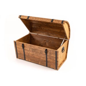 Könnte beinhalten: Eine Holzkiste mit einem gewölbten Deckel, der geöffnet ist, um das Innere zu zeigen. Die Truhe besteht aus gebeiztem Holz mit schwarzen Metallbändern und Beschlägen. Die Truhe ist für die Aufbewahrung konzipiert.
