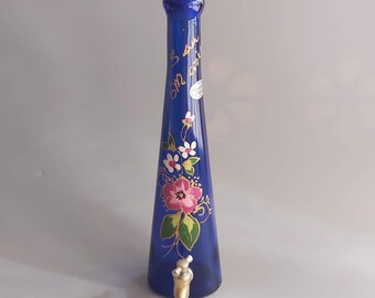 May include: A cobalt blue glass bottle with a gold painted floral design and a gold inscription that reads "5 years on this earth". The bottle has a gold metal spout.