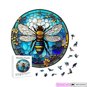 May include: A round wooden jigsaw puzzle featuring a stained glass style bee with blue, yellow, and black accents. The puzzle is set against a blue background with floral accents. The puzzle is labelled "Wooden Puzzle" and includes the difficulty level and size.