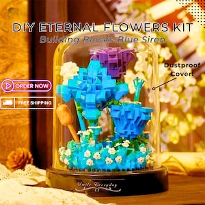 May include: DIY Eternal Flowers Kit building blocks in a glass dome with a blue, purple, and white flower arrangement. The dome has a black base with the words "Smile Everyday".