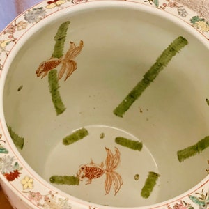 Peut inclure: Un pot en céramique blanche avec un motif floral vert et brun. Le pot a un large bord avec un motif floral et un motif vert et brun à l'intérieur. Le pot est décoré de deux poissons rouges et de bambou vert.