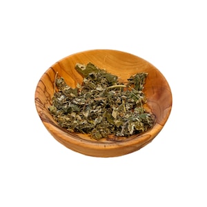 May include: Dried green leaves in a small wooden bowl. The bowl is light brown with a grain pattern.