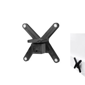 Könnte beinhalten: Schwarze Wandhalterung aus Kunststoff mit vier Schraubenlöchern und einer quadratischen Basis. Die Halterung ist X-förmig und hat ein kleines Loch in der Mitte der Basis.
