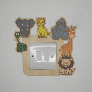May include: Wooden light switch cover featuring a jungle animal theme. The cover includes a gray elephant, yellow cheetah, blue gorilla, orange giraffe, and a lion. The light switch is white.