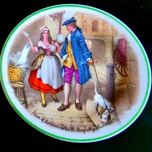May include: A round ceramic plate with a green rim featuring a colorful illustration of a person in a white and red dress and a person in a blue coat and pink breeches walking a spotted dog. The text Cries of London-Who'll Buy My Lavender is visible.