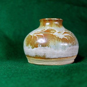 May include: A small, ceramic vase with a white and brown glaze. The vase has a rounded body and a slightly flared lip.