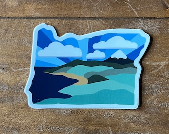 May include: A blue and white sticker of the state of Oregon with a mountain range and a body of water in the background. The sticker has a stylized sunburst design.