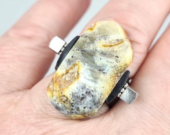 May include: A ring with a large, oval-shaped, light brown and gray stone set in a silver band. The stone has a unique, marbled pattern.
