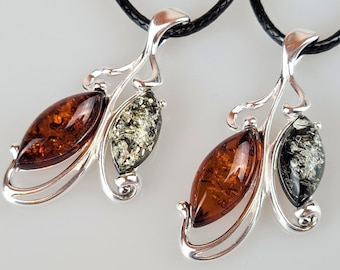 May include: Two silver pendants with amber stones. One pendant has a brown and green amber stone, the other has a brown and black amber stone.
